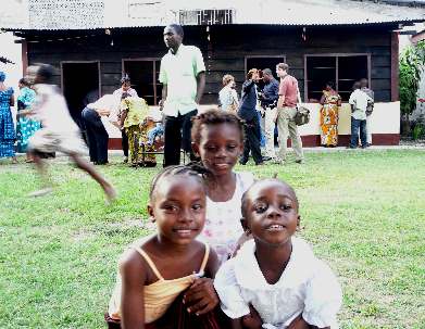 Au premier plan, trois petites filles scolarisées grâce à l’école communautaire. En arrière-plan, le chalet comportant les deux classes du complexe scolaire qui accueillent un total de 35 élèves.