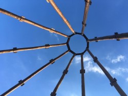 Les neuf mâts en bois qui formeront le dôme intérieur de la maison d’adoration sont couronnés par une structure en acier qui contiendra le plus grand nom, une fois le temple achevé.