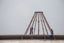 Les neuf mâts en bois qui formeront le dôme intérieur de la maison d’adoration sont couronnés par une structure en acier qui contiendra le plus grand nom, une fois le temple achevé.